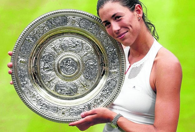 Garbiñe Muguruza posa, sonriente, junto a su primer trofeo de Wimbledon. Abajo, se abraza a Venus Williams.