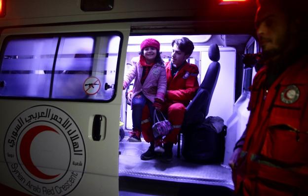 Una niña evacuada de la ciudad asediada de Duma, en Guta Oriental, se muestra sonriente junto a un sanitario de la Media Luna Roja. :: Bassam Khabieh / reuters/
